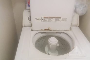 Laveuse à chargement par le haut usagée, couvercle ouvert, traces de rouille sur le rebord
