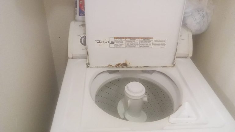 Laveuse à chargement par le haut usagée, couvercle ouvert, traces de rouille sur le rebord